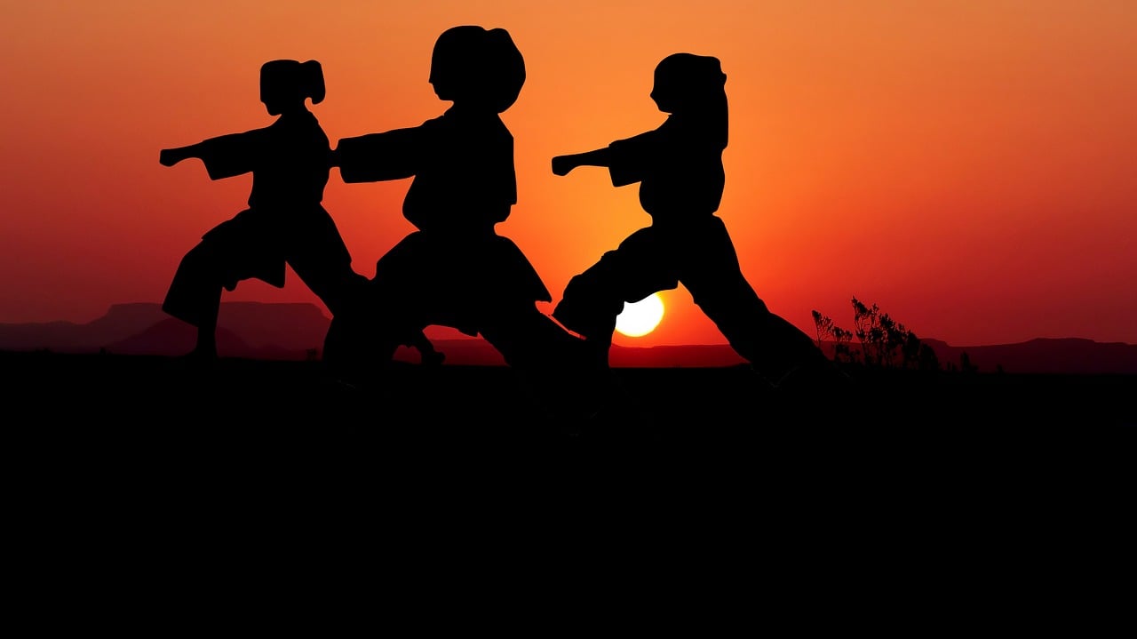 3 vrouwelijke karateka's oefenen kata voor de zonsondergang.